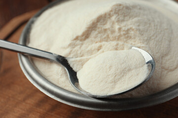 Bowl and spoon of agar-agar powder on wooden table, closeup