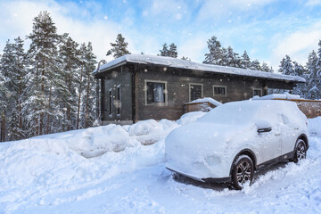 Fototapeta na wymiar A modern car buried in the snow in front of a cottage.