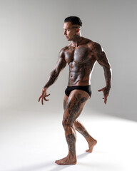 Young handsome bodybuilder posing,  athlete shows bodybuilding posing. hot tattoed man with beautiful body shows his muscles in the studio
