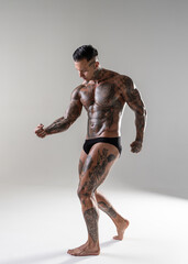 Fototapeta na wymiar Young handsome bodybuilder posing, athlete shows bodybuilding posing. hot tattoed man with beautiful body shows his muscles in the studio