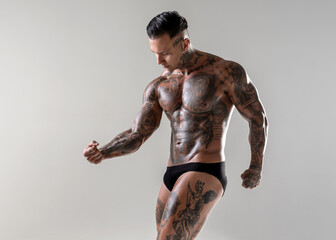 Young handsome bodybuilder posing,  athlete shows bodybuilding posing. hot tattoed man with beautiful body shows his muscles in the studio
