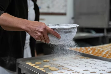 Tuinposter Cook adding powdered sugar to cookies as a topping © Nadja Knapp/Wirestock Creators