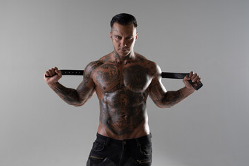 Handsome brutal man with tattoo holding belt and watching us. hot sportive guy in studio. bodybuilder. punisher