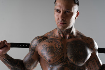 Muscular shirtless young man with whip in a mask.Brutal handsome man with tattooed body. Men tattoo casual fashion. Portrait of handsome male model. Muscular athletic sexy male with naked torso.