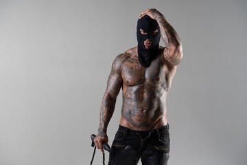Muscular shirtless young man with whip in a mask.Brutal handsome man with tattooed body. Men tattoo casual fashion. Portrait of handsome male model. Muscular athletic sexy male with naked torso.