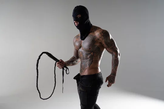 Muscular shirtless young man with whip in a mask.Brutal handsome man with  tattooed body. Men tattoo casual fashion. Portrait of handsome male model.  Muscular athletic sexy male with naked torso. Photos