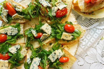 Flatten top view of plate with brusquettes of bread, roquefort cheese, arugula and cherry tomatoes