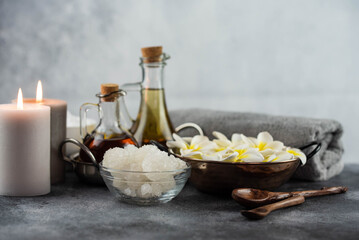 Spa massage relax composition setting. Natural essence oils, sea salt, towel, candles and plumeria frangipani exotic flowers. Gray colors.