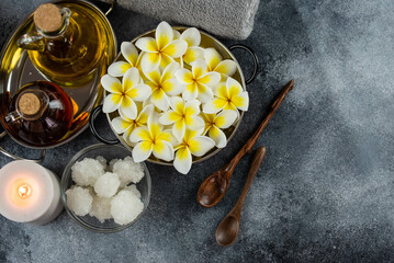 Fototapeta na wymiar Spa massage relax composition setting. Natural essence oils, sea salt, towel, candles and plumeria frangipani exotic flowers. Gray colors.