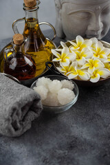 Spa massage relax composition setting. Natural essence oils, sea salt, towel, candles, Buddha head statue and plumeria frangipani exotic flowers. Gray colors.