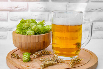 Mug with beer, fresh hops and ears of wheat on white wooden table