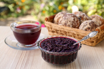 Elderberry (Sambucus) jam, glass cup of tea and tasty cookies on wooden table outdoors