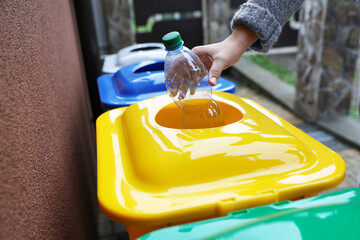 Woman throwing plastic bottle into recycling bin outdoors, closeup