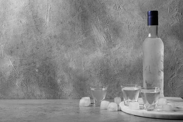 Bottle of vodka and shot glasses with ice cubes on table against grey wall. Space for text - obrazy, fototapety, plakaty