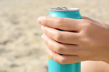 Woman holding aluminum can with beverage on sand, closeup. Space for text