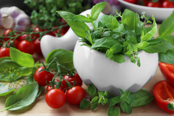 Mortar with fresh herbs, pepper and cherry tomatoes on wooden table, closeup