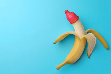 Banana with condom on light blue background, top view and space for text. Safe sex concept