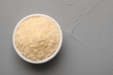 Delicious grated parmesan cheese in bowl on gray background. Space for text