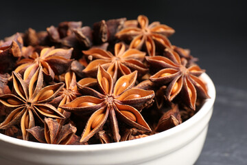 Bowl with aromatic anise stars on dark table, closeup