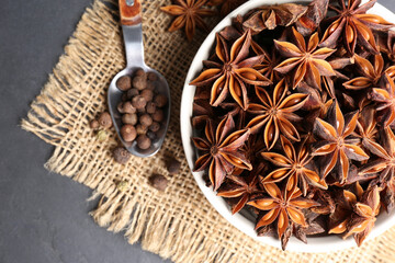 Bowl with aromatic anise stars and pepper on dark table, flat lay