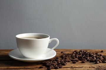 Cup of aromatic coffee and beans on wooden table. Space for text