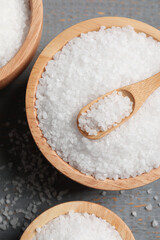 Bowls of natural sea salt on grey wooden table, flat lay