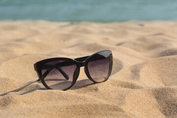 Stylish sunglasses on sandy beach near sea, closeup