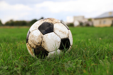 Dirty soccer ball on green grass outdoors, space for text