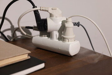 Smoking plug in power strip on wooden table, closeup. Electrical short circuit