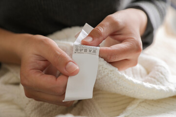 Woman holding clothing label on white garment, closeup