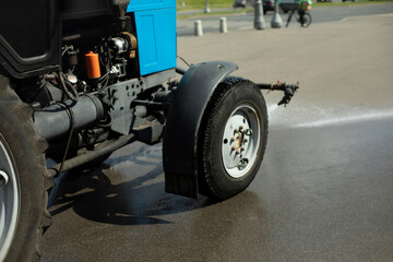 Fototapeta premium Car washes road. Tractor pours water. Washing off dirt from asphalt. Water jet from machine.