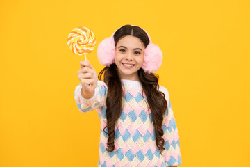 Funny child with lollipop over yellow isolated background. Sweet childhood life. Teen girl with yummy caramel lollipop, candy shop. Teenager with sweet sucker.