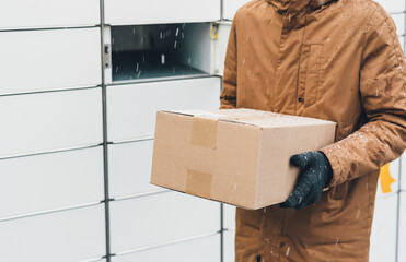 A man with a box in his hands near the self-service mail terminal. Parcel delivery machine. Person...