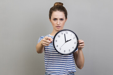 Portrait of bossy serious woman wearing striped T-shirt pointing finger at you holding in hand big...