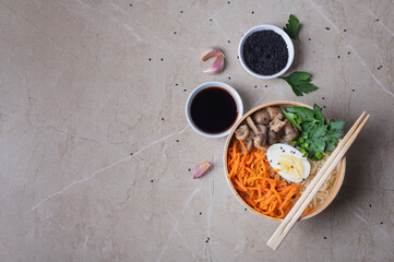 Noodle soup, ramen in a white bowl (bowl) with chicken egg, carrots, mushrooms on a light stone background.