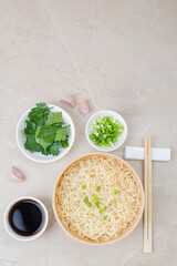 White bamboo plate (bowl) with egg noodles and plates with ingredients for it on a light background.