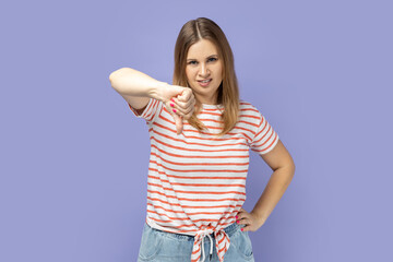 Portrait of sad upset attractive blond woman wearing striped T-shirt showing thumb down...