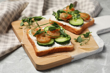 Tasty toasts with cream cheese, shrimps, cucumbers and microgreens served on grey marble table,...