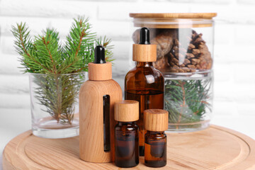 Bottles of essential oil, pine branches and cones on wooden board