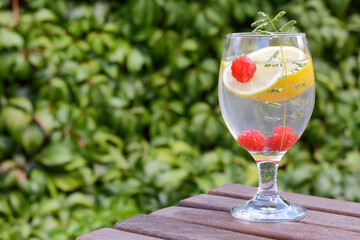 Delicious refreshing lemonade with raspberries on wooden table outdoors, space for text