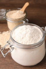 Jars with quinoa flour and seeds on wooden table, closeup