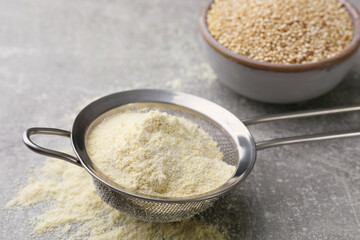 Sieve with quinoa flour on light grey table, closeup