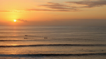 Amazing sunset at Uluwatu beach, where surfers and fishermen meet in the sea on dusk, Uluwatu, Bali, Indonesia.