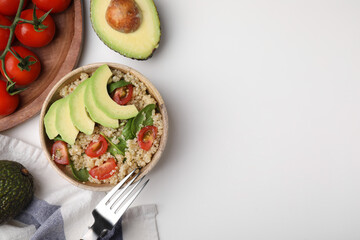 Delicious quinoa salad with tomatoes, avocado slices and spinach leaves served on white table, flat lay. Space for text