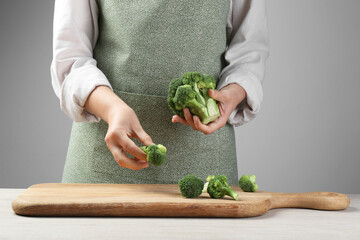 Woman with fresh broccoli at wooden table, closeup