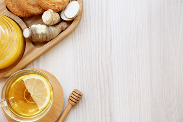 Cup of delicious tea with lemon, honey and ginger on white wooden table, flat lay. Space for text