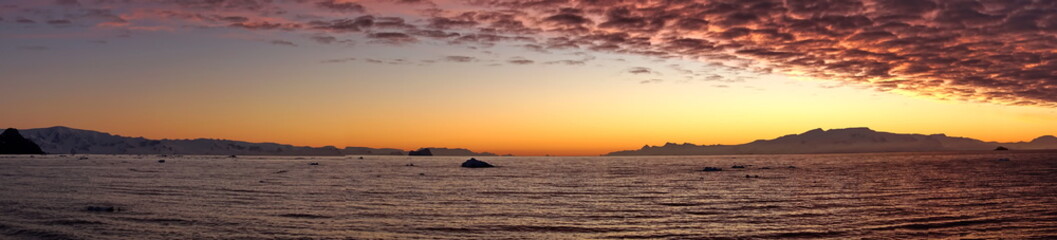 Fototapeta premium Popcorn clouds illuminated pink over the silhouette of a mountain, at sunset at Cierva Cove, Antarctica