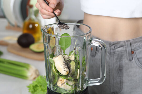 Woman adding chia seeds into blender with ingredients for green smoothie indoors, closeup