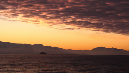Fototapeta premium Popcorn clouds illuminated pink over the silhouette of a mountain, at sunset at Cierva Cove, Antarctica