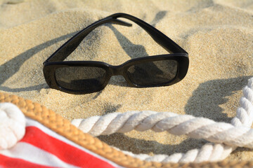 Stylish sunglasses and beach bag on sand, closeup